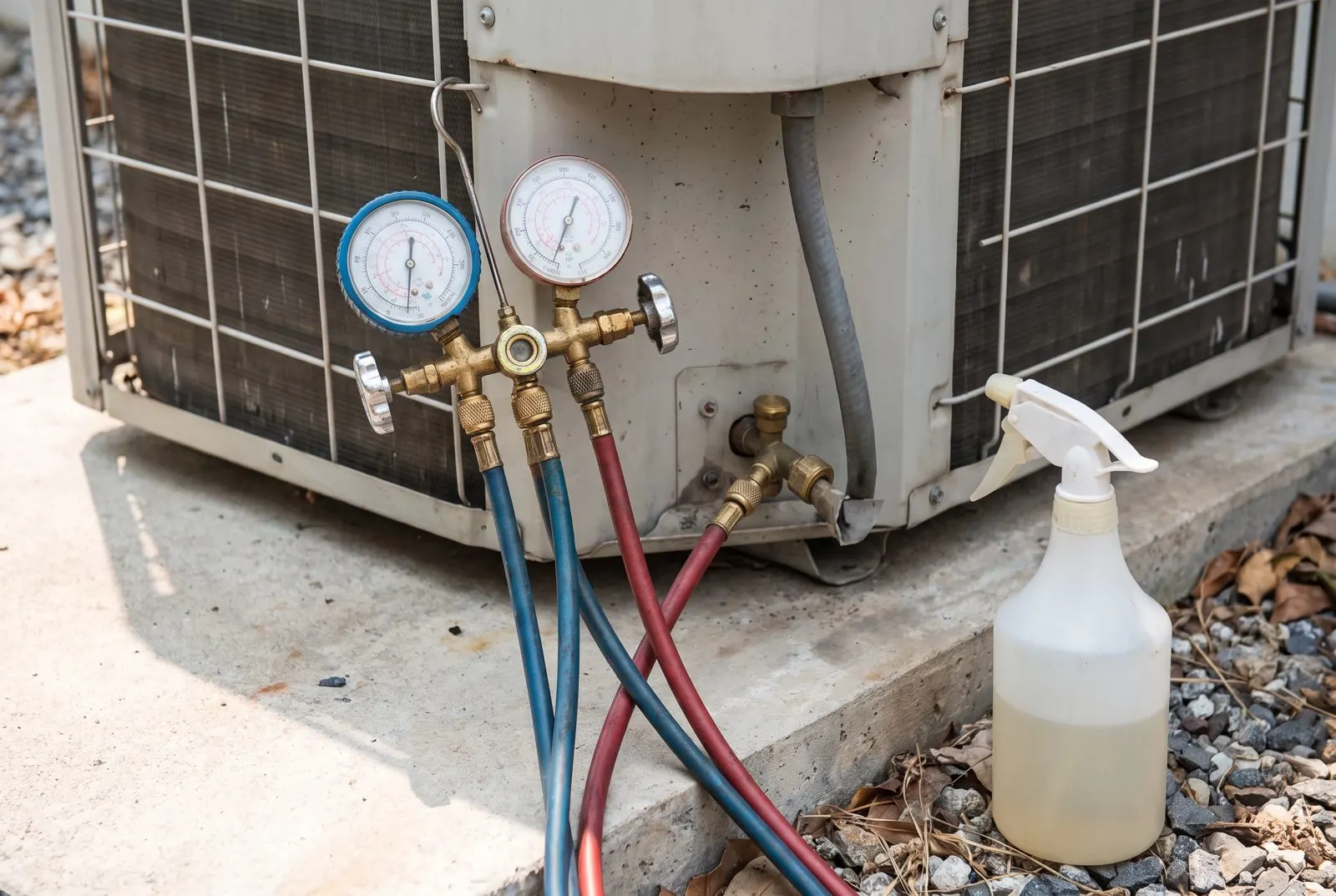 Refrigerant gauges hooked to an outdoor unit beside a spray bottle